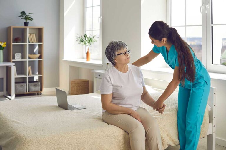 Older adults share conversation at a small table in a bright assisted living common room.
